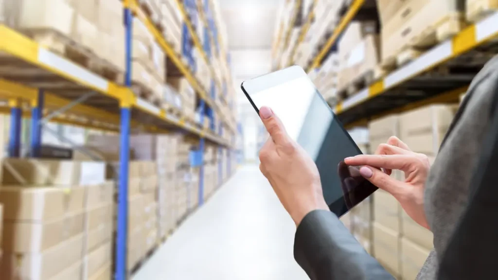 RFID solutions in retail for real-time warehouse inventory management Hand using a tablet in a warehouse aisle, demonstrating RFID solutions in retail for real-time inventory tracking.